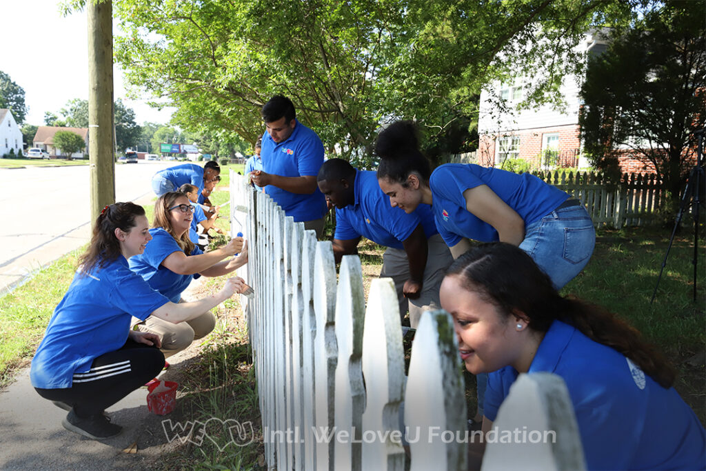 Volunteers painting Ms. Monroe's white-picket fence