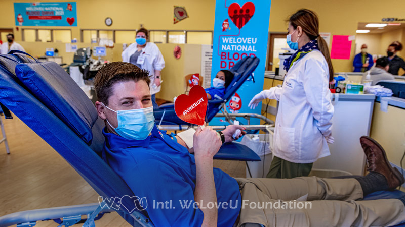 A volunteer holds a sign that says #DonateLove while donating blood