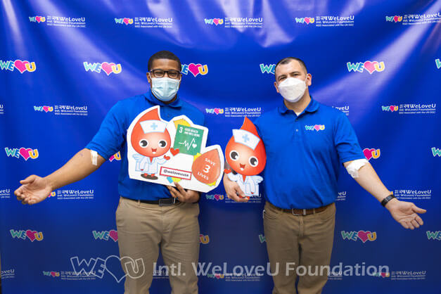 Two WeLoveU volunteers show their arm they donated blood with