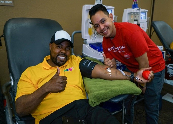 A WeLoveU Foundation volunteer donates blood and smiles next to a LifeStream BloodBank phlebotomist